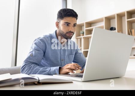 Focused young Arab employee man in casual typing on laptop Stock Photo