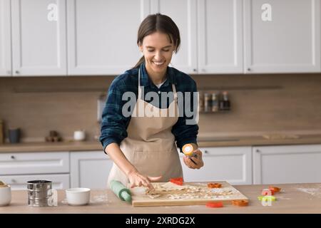 Cheerful young baker woman wearing apron, baking in kitchen Stock Photo
