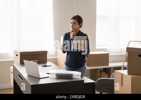 Serious Indian female, warehouse worker using tablet working online Stock Photo