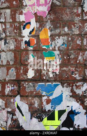 closeup shot of a brick wall covered in layers of torn and peeling advertising poster Stock Photo
