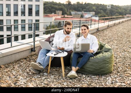 Two colleagues working on laptops outdoors on a rooftop Stock Photo