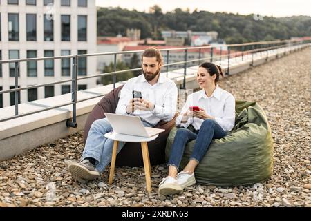 Two people working remotely with gadgets on rooftop Stock Photo