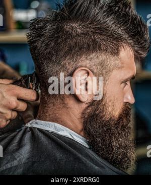 Hipster client getting haircutthe back of the head. Hands of barber with hair clipper, close up. Haircut concept. Man visiting hairstylist in Stock Photo