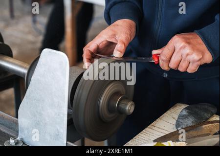 male sharpener sharpens a knife blade on a knife sharpening machine in workshop Stock Photo