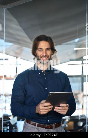 Vertical portrait of male company executive using digital tablet standing in office. Stock Photo