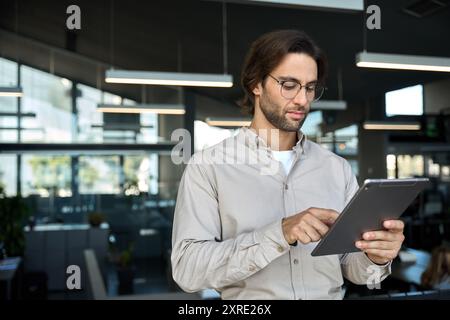 Serious busy young European business man using tablet standing in office. Stock Photo