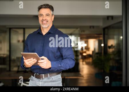 Smiling mature business man executive standing in office with tablet. Portrait Stock Photo