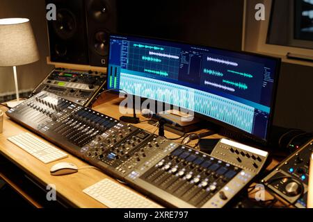 Professional recording studio featuring mixing consoles, monitor speakers, and computer displaying audio editing software. Spacious desk creating environment suitable for sound engineering Stock Photo