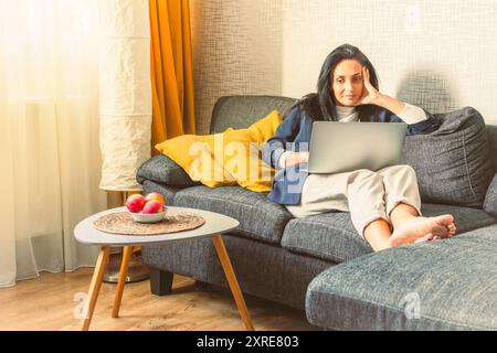 Young caucasian modern brunette business woman in suit sit lay at home on couch scroll do shopping use laptop on lap in cozy modern living room house Stock Photo