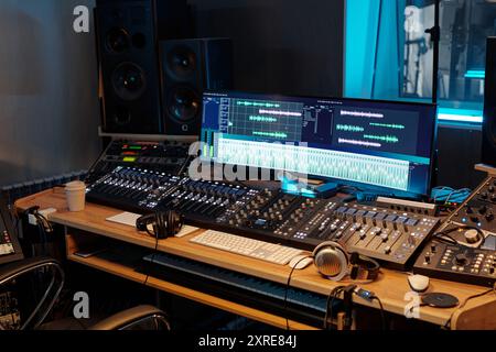 View of professional recording studio with various audio mixing consoles, headphones, and computer screens displaying audio tracks, blue accent lighting illuminating studio space Stock Photo