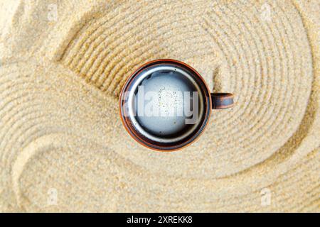 Clay cup of coffee on white sand with a pattern of wave lines in Japanese style. Harmony, leisurely, meditation, zen concept. Stock Photo
