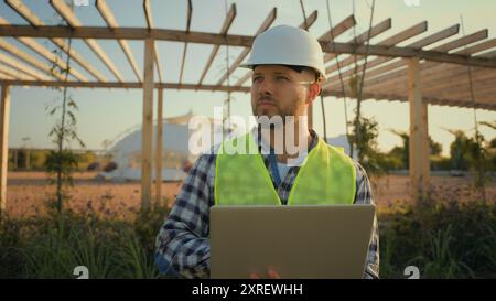 Thoughtful Caucasian male man experienced worker inspector helmet hardhat guy engineer technician typing laptop computer entering data internet pc Stock Photo