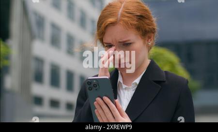 Nervous sad Caucasian redhead businesswoman female girl woman student worker entrepreneur using mobile cell phone cry anxious fired job problems Stock Photo
