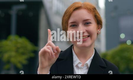Young puzzled thoughtful Caucasian red haired businesswoman lady female woman thinking having creative new idea plan raise finger insight eureka Stock Photo