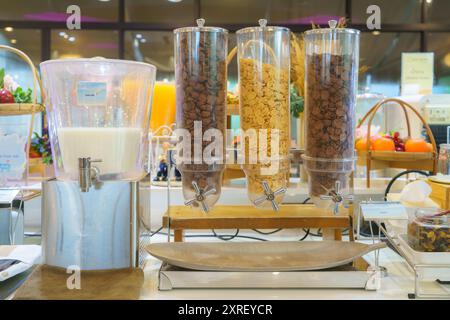Breakfast setup featuring a cereal dispenser with three compartments filled with different types of cereals. Stock Photo