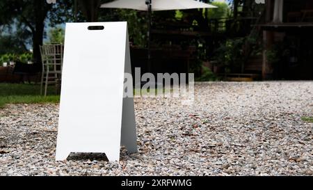 A blank white signboard standing on a gravel-paved surface, offering ample space for customized text or branding. Stock Photo