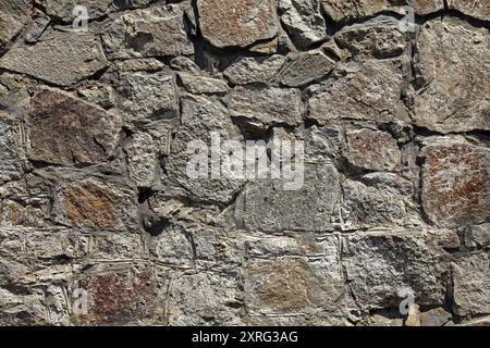 Granite wall, background. Surface of stone structure built of granite rocks (bricks). The wall texture of volcanic grey color. Fence large blocks Stock Photo