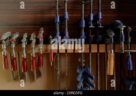 Various types of clamps and tools hanging on wooden wall in workshop, suggesting organized and accessible workspace for woodwork and craftsmanship Stock Photo
