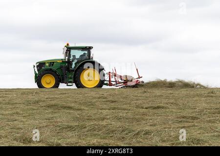 Farmer in tractor cutting grass in hay field or meadow to make feed for livestock during late summer, Hampshire, England, UK Stock Photo