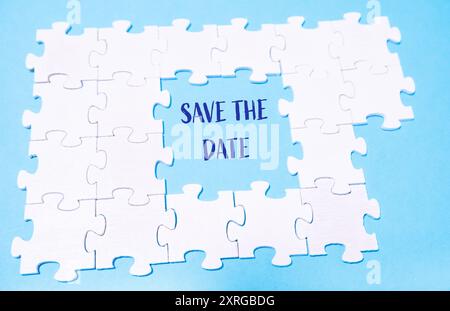 A puzzle with the word save the date written in the middle. The puzzle is made up of white pieces and is scattered across the image Stock Photo