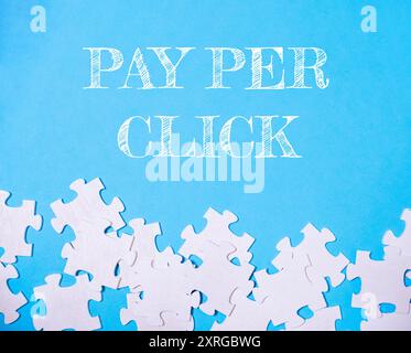 A blue background with white jigsaw puzzle pieces scattered on it. The puzzle pieces are arranged in a way that they spell out the word pay per click Stock Photo