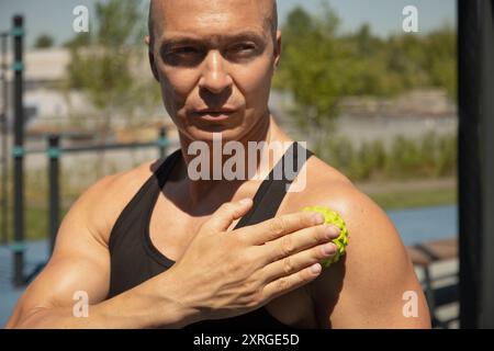 Athletes man is massaging his shoulder by spiky massage ball techniques for tense after active workout. Close up. Myofascial release. Stock Photo