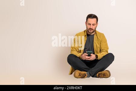 Serious young handsome businessman reading text messages on smart phone while sitting with legs crossed. Male professional dressed in casuals checking Stock Photo
