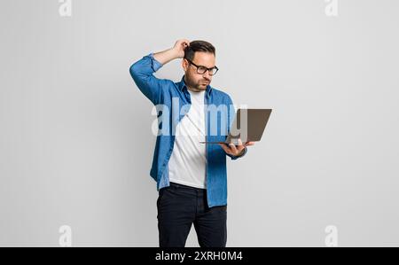 Confused disappointed businessman with hand in hair reading e-mail over laptop on gray background Stock Photo