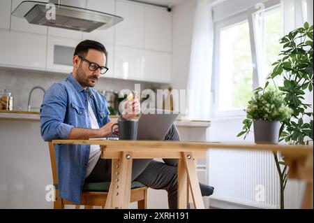 Serious young businessman paying through credit card while shopping online on laptop in home office Stock Photo