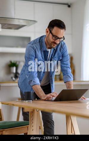 Focused young businessman with glasses on working online over laptop on desk at cozy home office Stock Photo