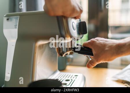 Close-up of hands operating an espresso machine in a cozy kitchen setting. Stock Photo
