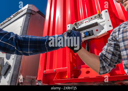 Two workers shake hands in front of a red shipping container, symbolizing collaboration in logistics. Stock Photo