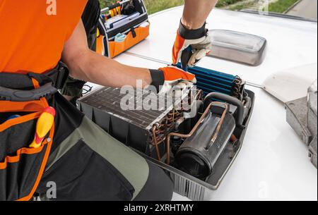 A technician adjusts components of a rooftop RV Camper HVAC unit, using tools from an open toolbox, while working on a building. Stock Photo