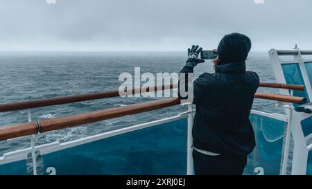 Antarctica Cruise Ship Passenger with Mobile Phone Takes Photo of A23a World's Largest Iceberg Drake Passage Ice in Distance Moody. Female Tourist Stock Photo