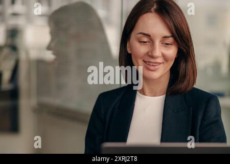 A professional woman is focused on her work, using a laptop in an office setting Stock Photo
