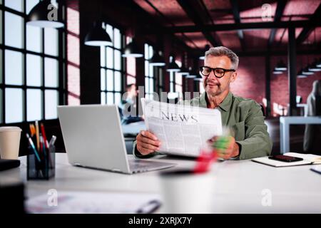 Businessman Reading Newspaper At Office Desk At Work Stock Photo