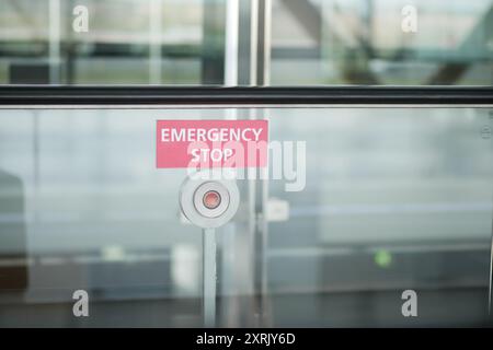 An emergency stop button is placed on a glass wall in a public space for safety measures Stock Photo