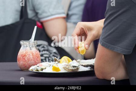 Midsection of man holding slice of lemon and eating fresh mussels from metal tray with ice chips in the farmers market. Stock Photo