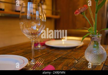 Elegant table setting in a cozy restaurant with empty wine glass, white plate, and silver cutlery on rustic wooden table Stock Photo