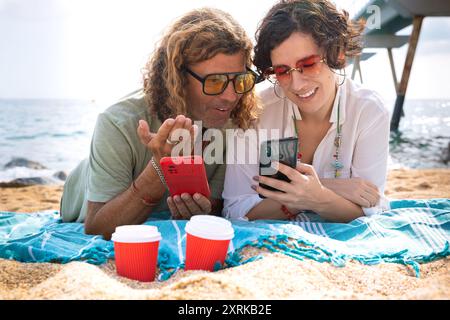 Smiling couple on the beach browsing smartphone apps. Stock Photo