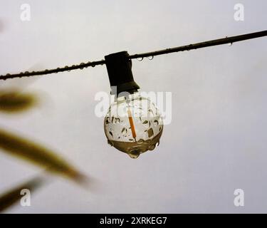 garden lights showing a single bulb with raindrops on, UK summer 2024, set against a grey sky with a texture overlay Stock Photo