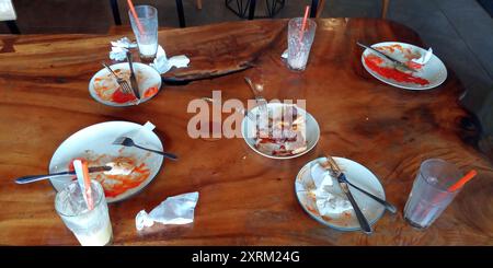 The leftover food and dirty empty dishes on the restaurant table. symbolize the end of lunch or dinner. Scraps left over after the party. Stock Photo