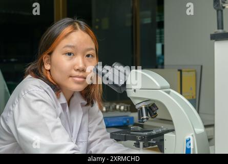 Cute scientist schoolgirl in lab coat is using microscope for study microbiology in laboratory.  Kid learning science education Stock Photo