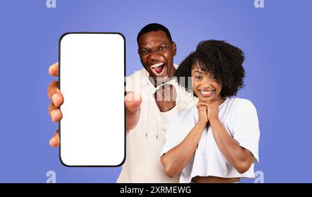 Excited Couple Holding Smartphone With Blank Screen on Purple Background Stock Photo