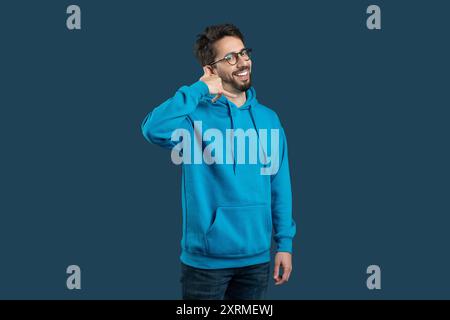 Friendly Man In Blue Hoodie Smiling While Making Call Gesture Stock Photo