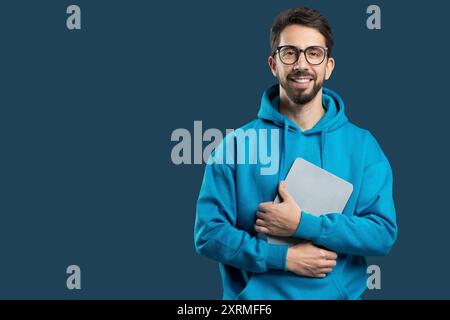 Young Man in Blue Hoodie Holding Laptop With Confident Smile Stock Photo