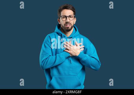 Young Man Wearing Blue Hoodie Expresses Emotion Over Dark Background Stock Photo