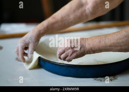 Old grandmother putting rolled dough in a pan. Elderly woman making traditional balkan pie Stock Photo