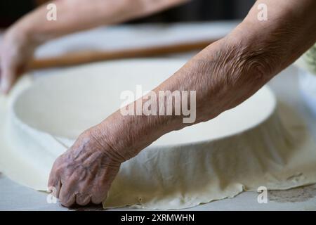 Old grandmother putting rolled dough in a pan. Elderly woman making traditional balkan pie Stock Photo