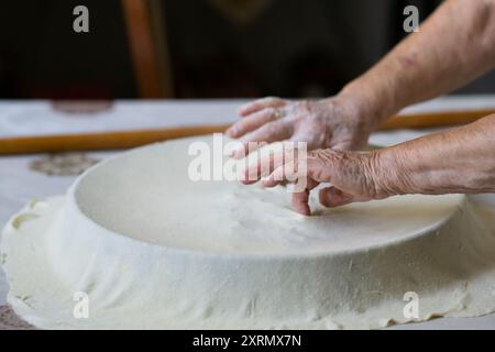 Old grandmother putting rolled dough in a pan. Elderly woman making traditional balkan pie Stock Photo